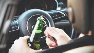 Driver opening a beer bottle behind the wheel