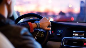 A person driving a car with one hand on the steering wheel