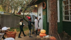 Three children in costumes approach the front door of a home to trick-or-treat on Halloween.