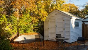 An outdoor shed with a small boat lying next to it on the ground.