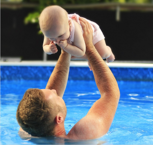 Man holding baby above pool